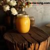 A jar of golden honey sits on a rustic wooden surface, surrounded by decorative flowers in a softly lit room.