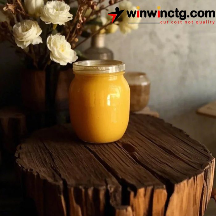 A jar of golden honey sits on a rustic wooden surface, surrounded by decorative flowers in a softly lit room.